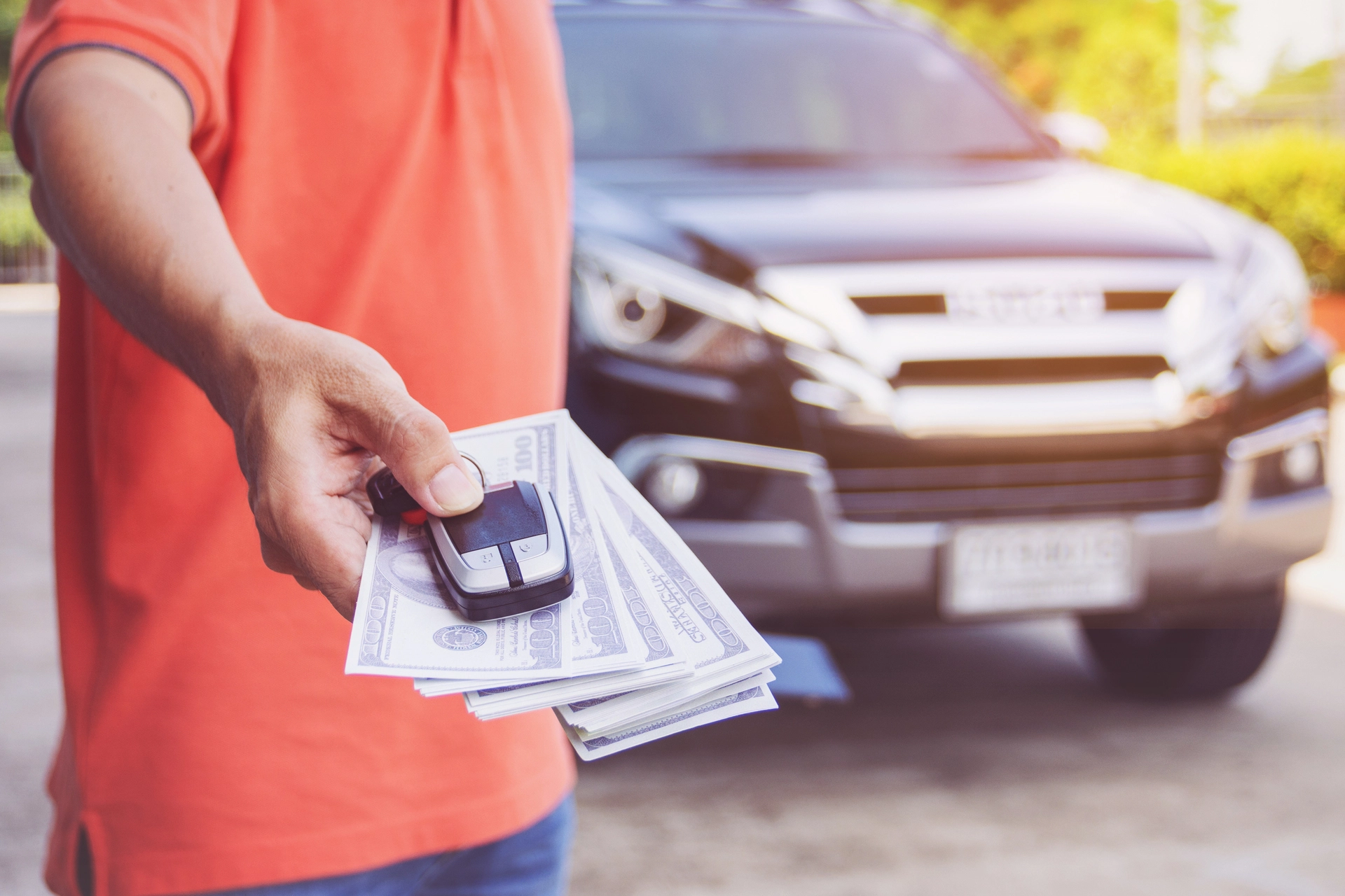 Hand holding car keys and cash in front of a car to show how to find the value of a car