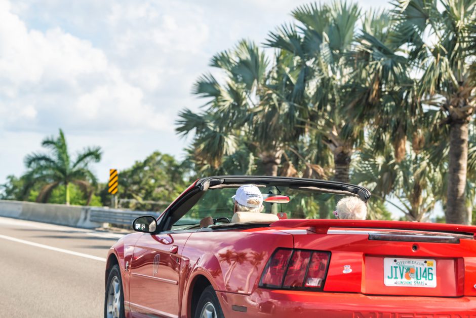 Ellenton, USA - April 27, 2018: Senior couple driving on sports car on road, highway with palm trees in Florida